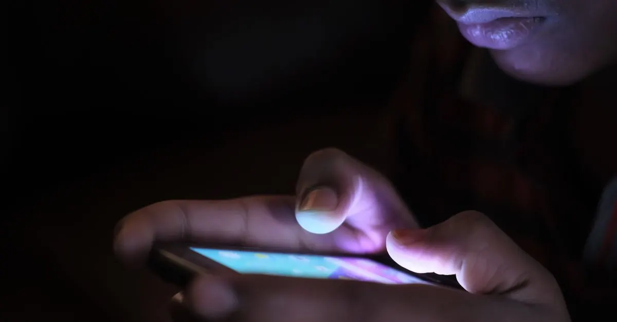 A person in a dark room looking at a lit-up smartphone screen